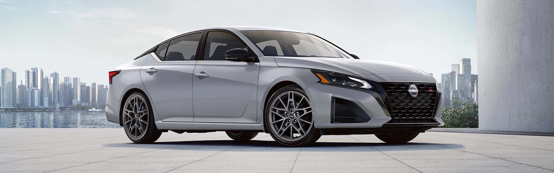 A silver Nissan Altima in front of a city skyline.
